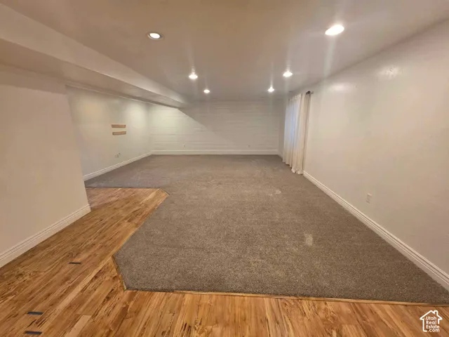 Spacious room featuring wood-finish flooring, wall-to-wall carpeting, recessed lighting, and a white horizontal shiplap accent wall