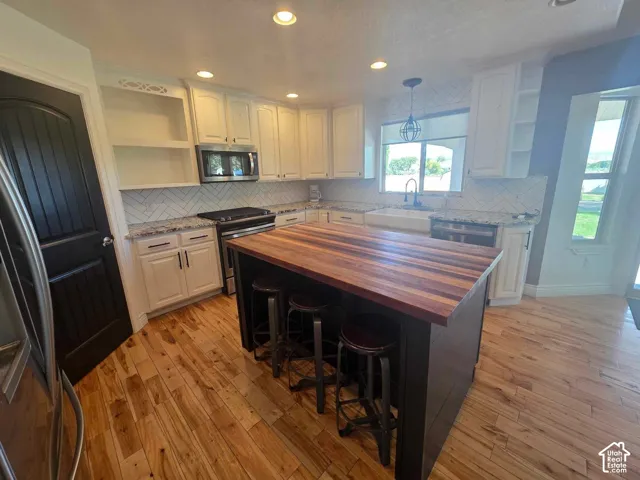 Kitchen featuring a center island with a wood-finish countertop, white shaker-style cabinetry, herringbone-pattern tile backsplash, farmhouse-style apron sink, and natural wood-finish flooring