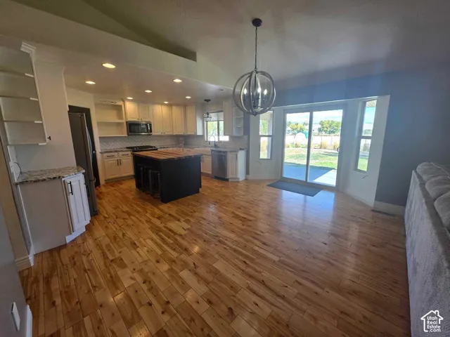 Open-concept kitchen and living area featuring wood-finish flooring, a central island with a wood countertop, white cabinetry, a spherical pendant light fixture, and sliding glass patio doors