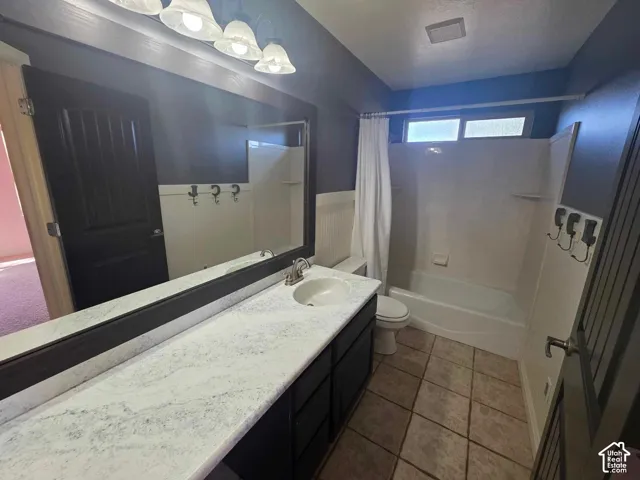 Bathroom featuring a vanity with stone-finish countertop and integrated sink, large-format tiled flooring, full-width wall mirror, beadboard wainscoting, and a tub-shower combination