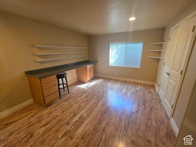 Wood-finish flooring, built-in desk with laminate surface and cabinetry, wall-mounted shelving, recessed lighting, and six-panel interior door
