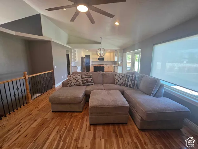 Vaulted ceilings, wood-finish flooring, metal spindle railing, ceiling fan, and large picture window