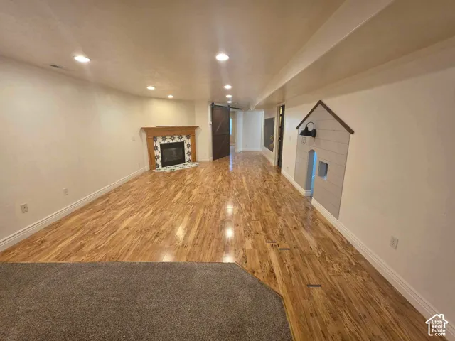 Wood-finish flooring, fireplace with decorative tile surround and wooden mantel, recessed lighting, and barn-style door