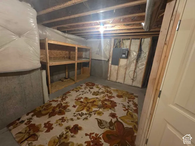 Unfinished storage area featuring exposed wood-stud framing, concrete foundation walls, built-in wooden shelving, and an electrical service panel