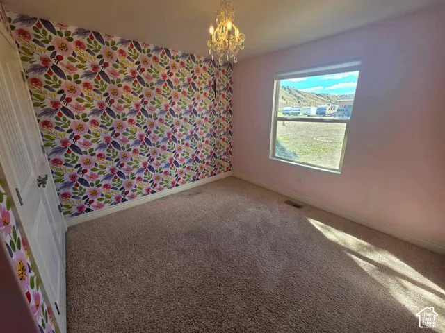 Interior space featuring patterned floral wallpaper, carpeted flooring, a multi-tiered crystal-style chandelier, and a single-pane window with mountain landscape backdrop