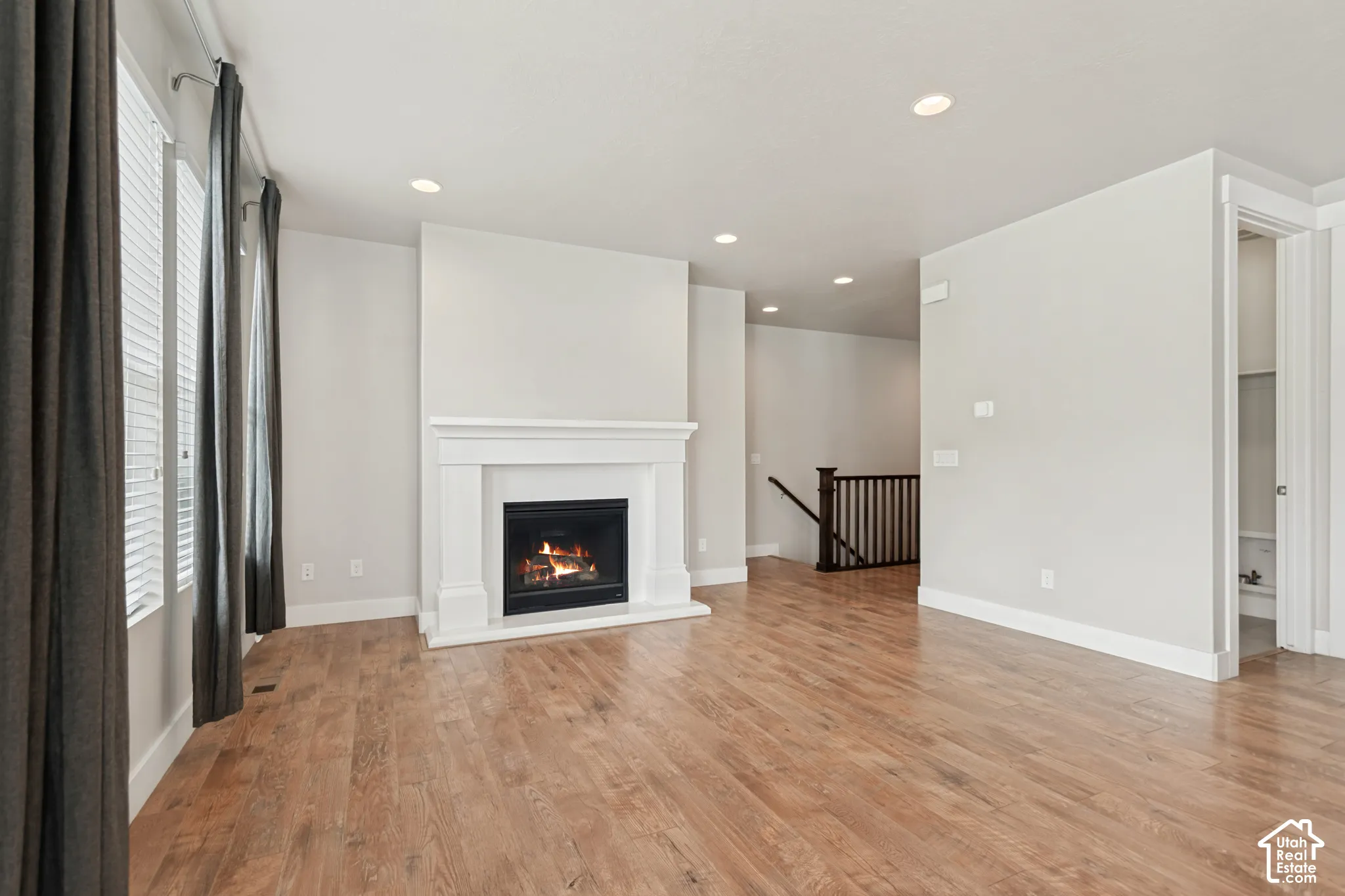 Living area featuring wood-finish flooring, a white-mantel fireplace, recessed lighting, and vertical windows
