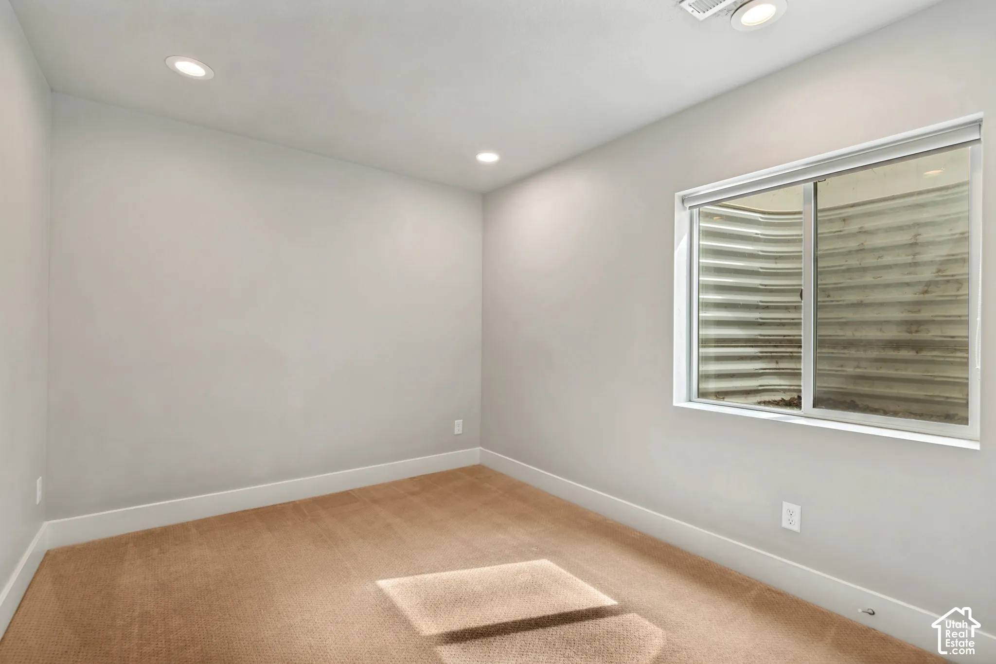 Interior room featuring neutral-toned carpeting, recessed lighting, and a slider window with an integrated egress well