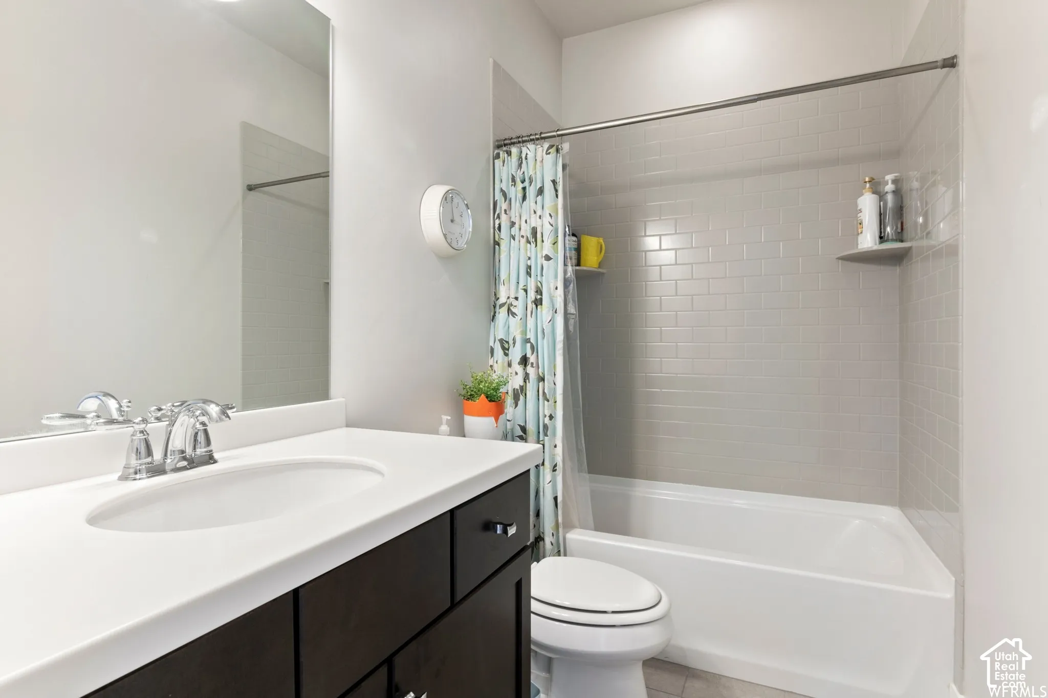 Bathroom featuring a dark wood-finish vanity, solid surface countertop, chrome faucet, wall-to-wall vanity mirror, and a tub-shower combination with subway-style wall tile