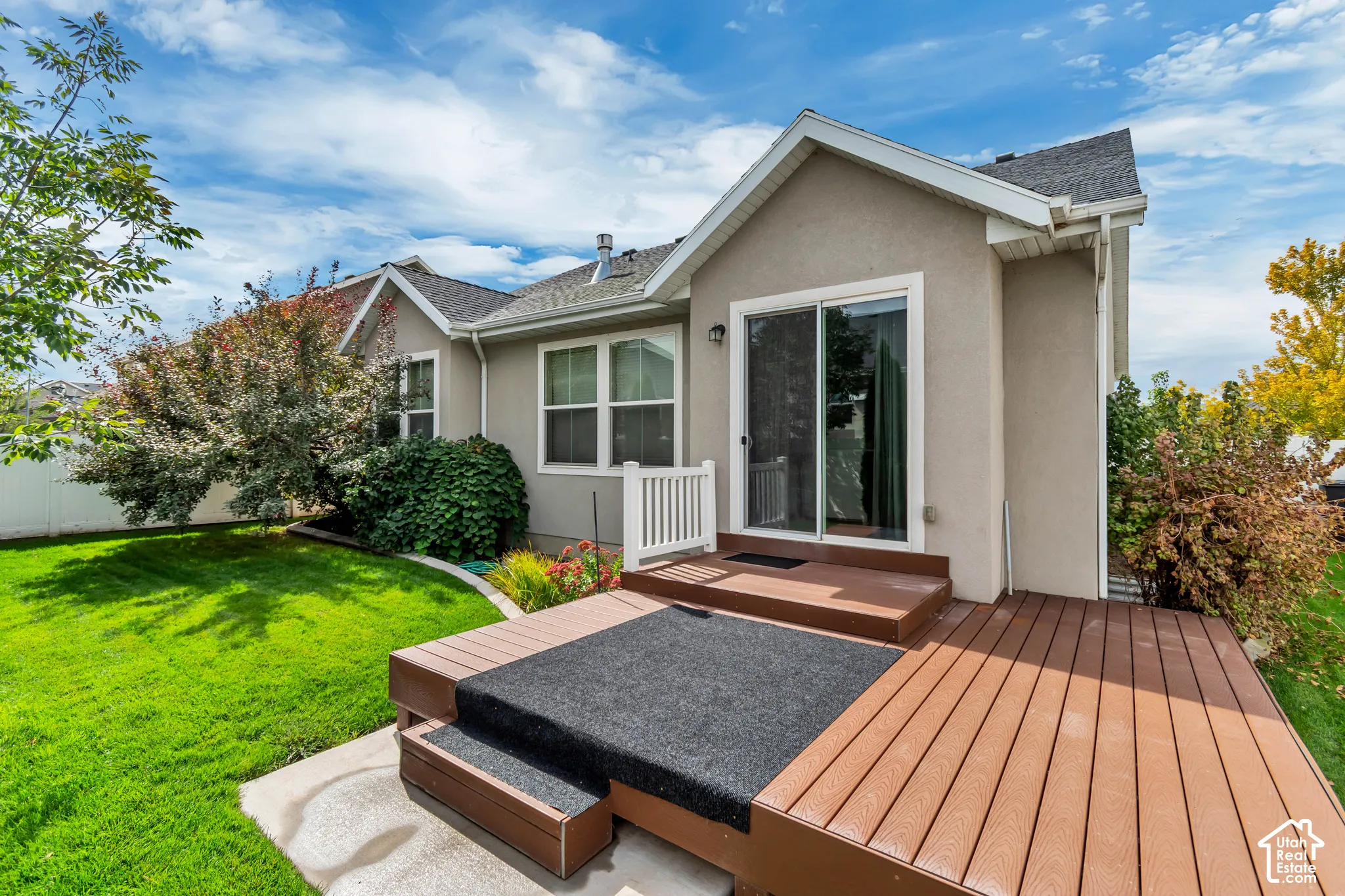 Stucco exterior featuring a multi-level composite deck, white railing, glass sliding doors, and a manicured lawn