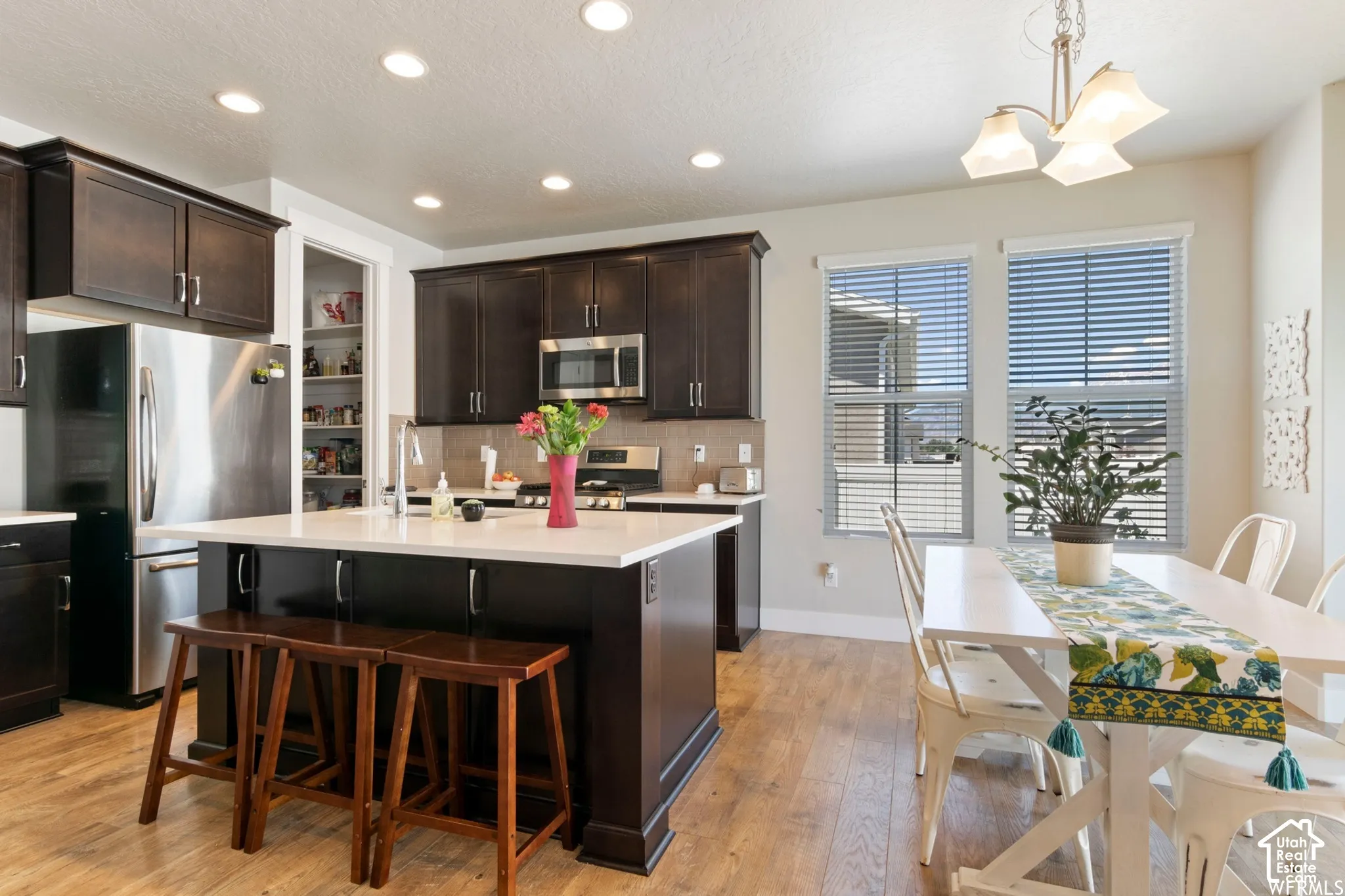 Kitchen featuring dark-finish cabinetry, central island with light-toned solid surface countertops, stainless steel appliances, and wood-finish flooring