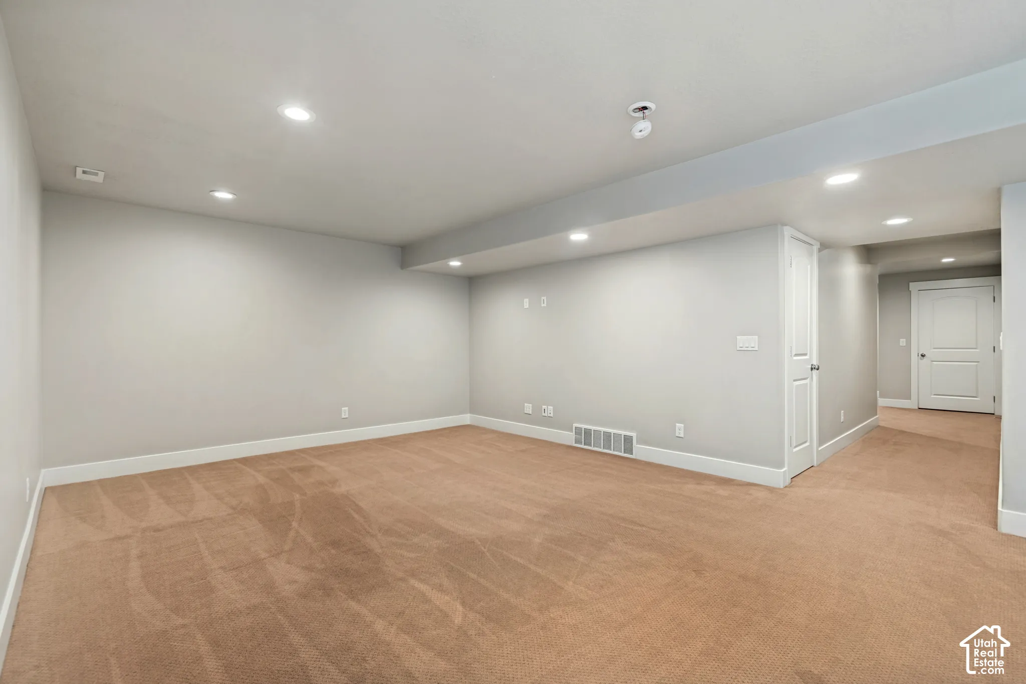 Neutral-toned interior space featuring recessed ceiling lighting, wall-to-wall carpeting, and a multi-panel interior door