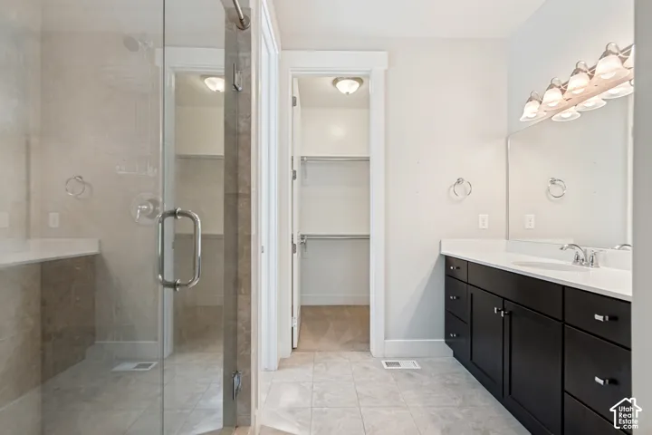 Bathroom featuring a glass-enclosed shower with tile surround, dark-finish cabinetry, solid-surface countertop, multi-light vanity fixture, and walk-in closet