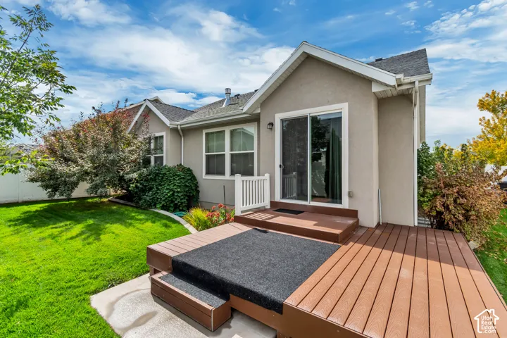 Stucco exterior featuring a multi-level composite deck, white railing, glass sliding doors, and a manicured lawn