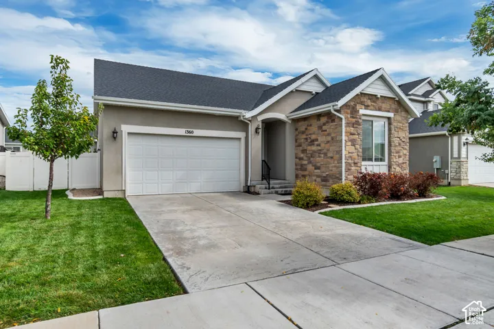 Single-story exterior featuring a stone facade, gabled roofline, attached two-car garage, and concrete driveway
