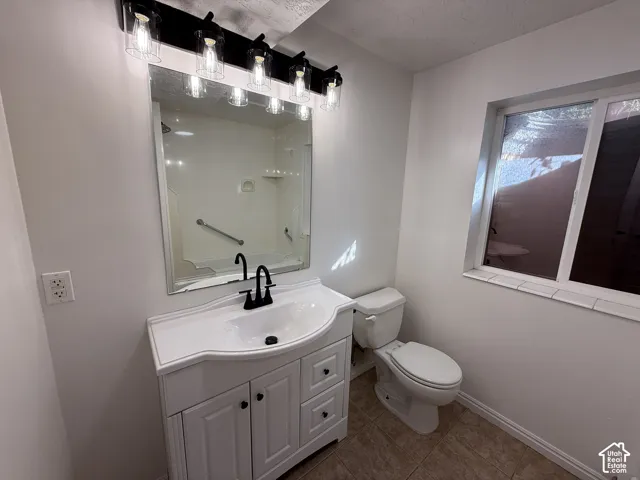 White vanity cabinet with an integrated basin, matte black faucet, full-width mirror, five-light fixture with clear glass shades, and neutral floor tile
