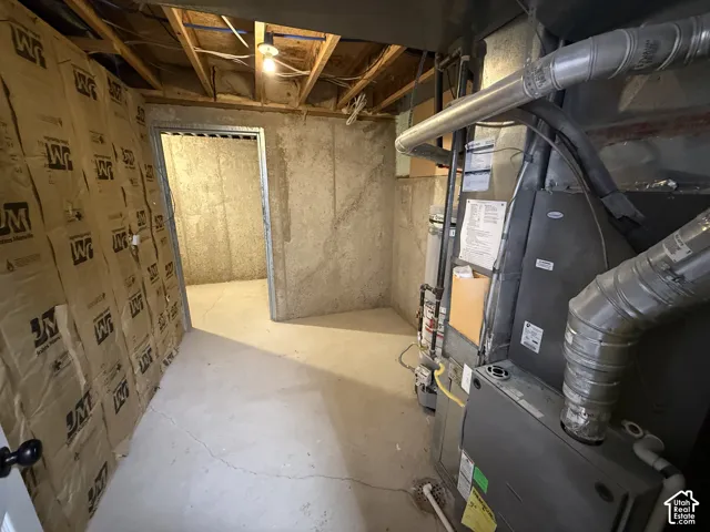 Utility space featuring a concrete floor, exposed structural joists, fiber insulation, and a mechanical system