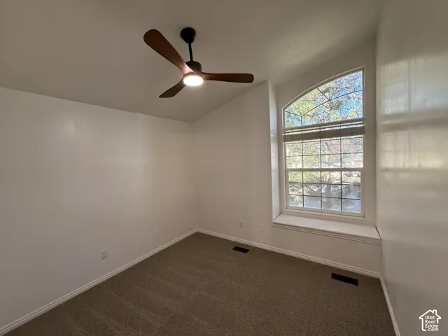 Vaulted ceiling room featuring neutral carpeting, a modern three-blade ceiling fan with integrated lighting, and an arched window with a built-in sill
