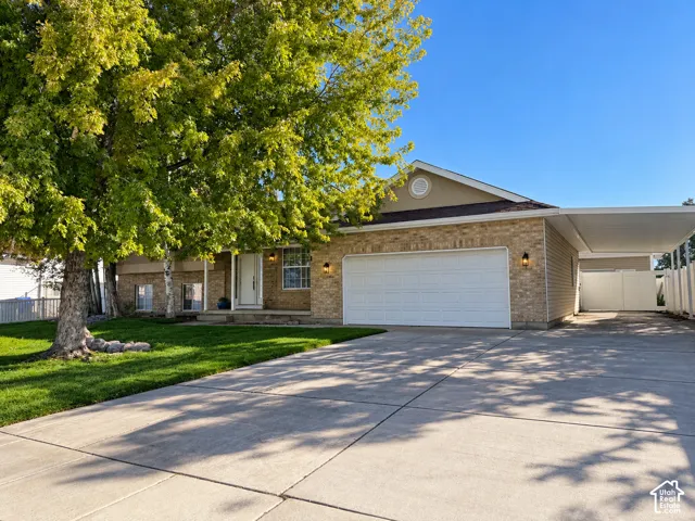 Brick exterior featuring a concrete driveway, attached garage, side carport, and mature landscaping