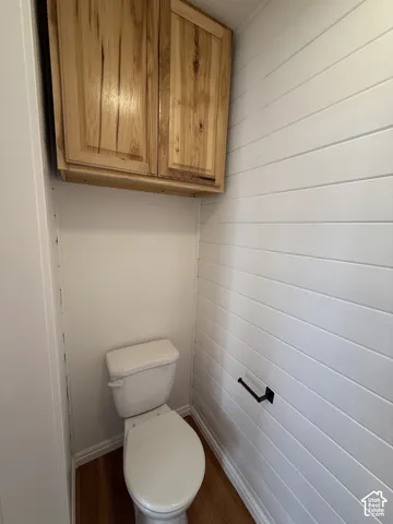 Custom natural wood-finish upper cabinetry, white horizontal plank wall detailing, matte black toilet paper holder, and wood-finish flooring
