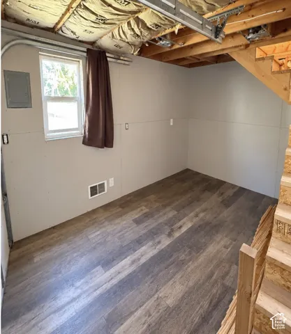 Finished space featuring wood-finish flooring, drywall walls, an exterior-facing window, and exposed wood-frame staircase