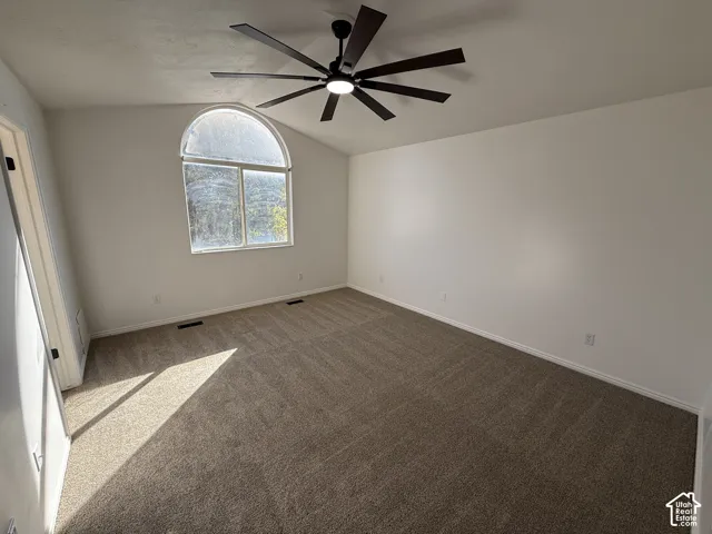 Vaulted ceilings featuring an arched window and a multi-blade ceiling fan with integrated lighting, finished with neutral-tone carpeting