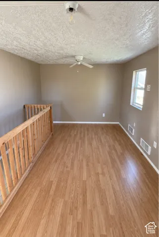 Wood-finish flooring, textured ceiling, ceiling fan, and natural wood balustrade railing