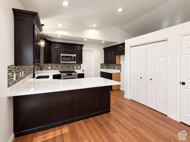 Kitchen featuring dark cabinetry, stone-finish countertops with a peninsula, mosaic tile backsplash, stainless steel microwave, and wood-finish flooring