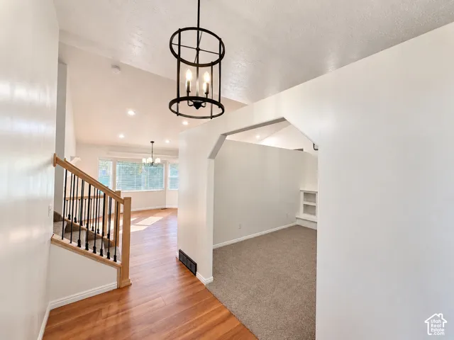 Interior featuring wood-finish flooring, a tiered staircase with wood handrails and black metal spindles, an open-concept archway, a metal drum pendant light, and built-in shelving