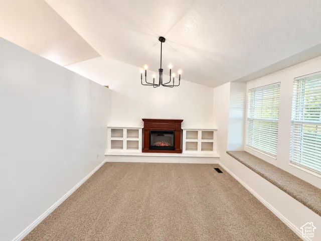Vaulted ceiling, built-in fireplace with wooden mantel, custom recessed cabinetry, and a carpeted window seat