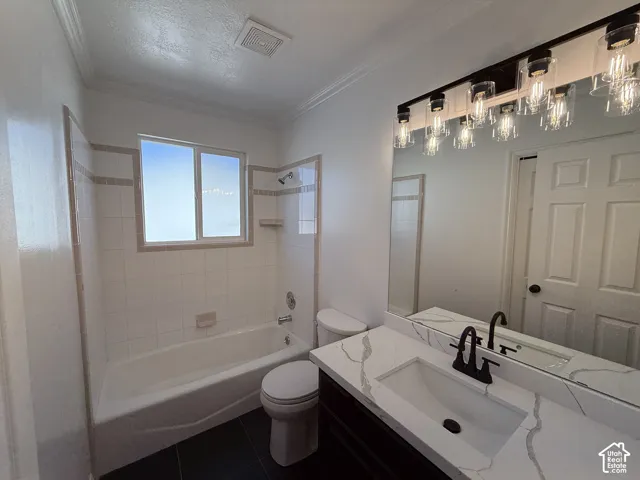 Bathroom featuring a vanity with a white countertop and dark cabinetry, undermount sink with matte black faucet, wall-to-wall mirror, industrial-style multi-light fixture, and a tiled shower-tub enclosure