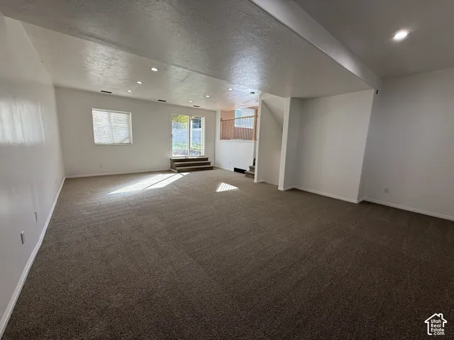 Neutral-toned interior space featuring recessed ceiling lighting, carpeted flooring, a sliding glass door, and a wooden staircase railing