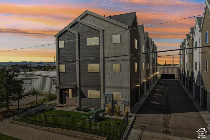 Contemporary multi-story exterior featuring a mix of horizontal siding and textured stucco, metal roof accents, attached garages, and a fenced front yard