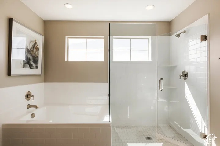 Bathroom featuring a soaking tub with white subway tile surround, a glass-enclosed shower with built-in shelving, two multi-pane windows, and recessed lighting