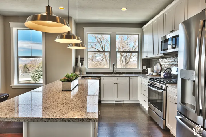 Kitchen featuring a granite-topped center island, custom white cabinetry, stainless steel appliances, dark brick backsplash, and wood-finish flooring
