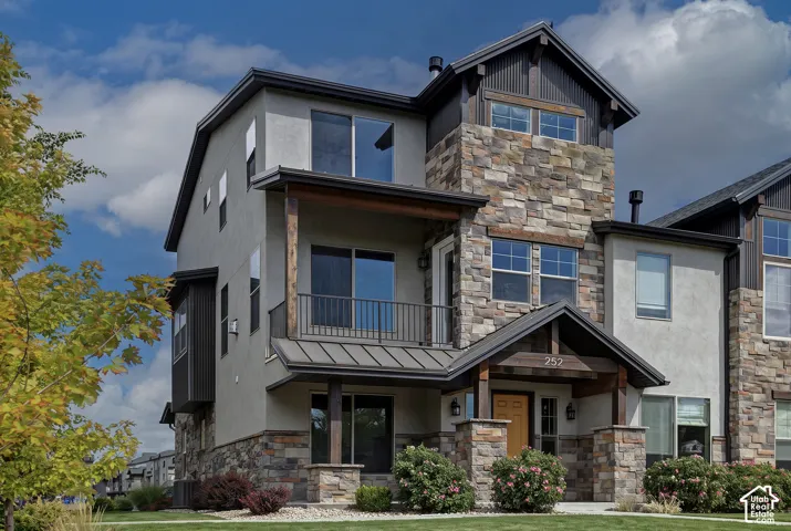 Multi-level exterior featuring stone veneer accents, stucco siding, a metal roof porch covering, a covered balcony with metal railing, and exposed wood beam detailing