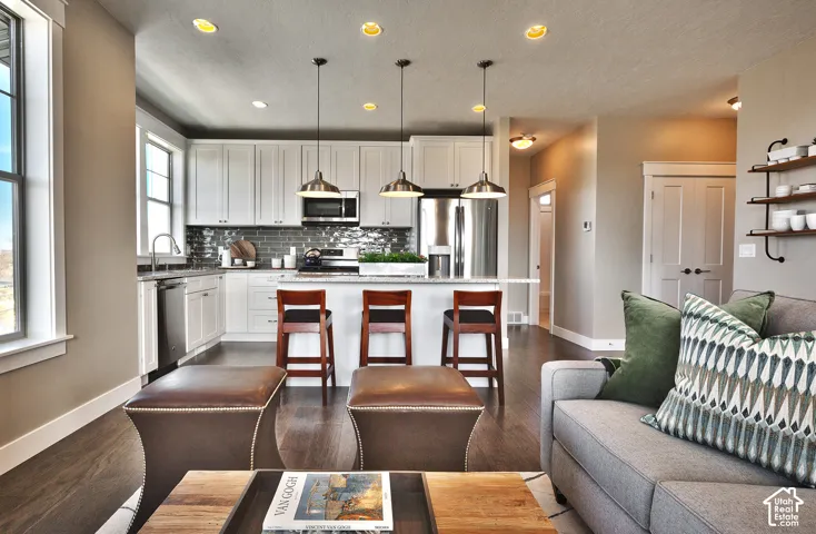 Kitchen featuring white cabinetry, stone-finish countertops, subway tile backsplash, recessed ceiling lighting, and three pendant lights over the central island
