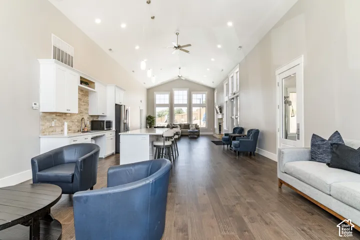 Open-concept interior featuring vaulted ceilings, recessed lighting, wood-finish flooring, a kitchen island, and custom cabinetry with stone-finish backsplash