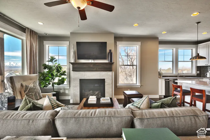 Fireplace with stone-style surround and wood mantel, recessed lighting, ceiling fan, and large windows with mountain scenery
