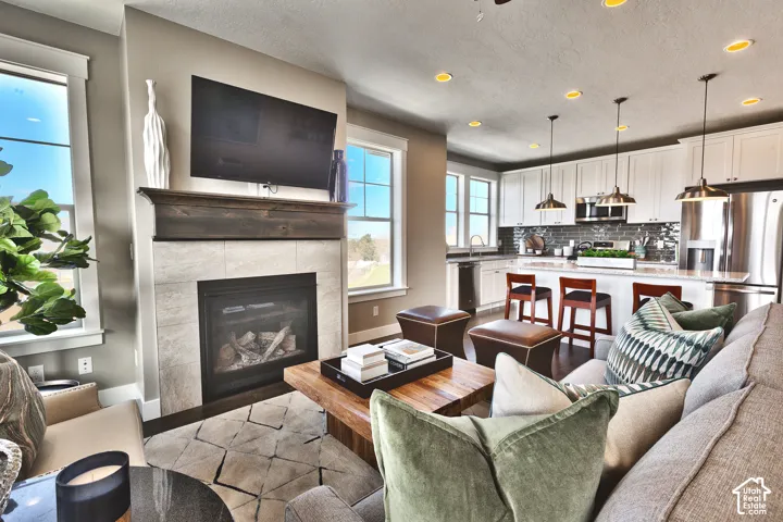 Fireplace featuring a stone tile surround and a wood mantel, open-concept kitchen with white cabinetry, stainless steel appliances, quartz countertops, and industrial-style pendant lighting