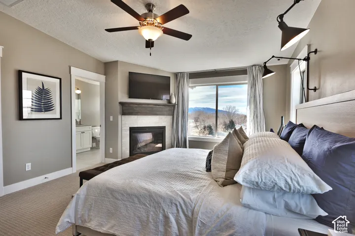 Fireplace with a stone surround and rustic wood mantel, ceiling fan with integrated lighting, wall-mounted adjustable sconces, and mountain backdrop
