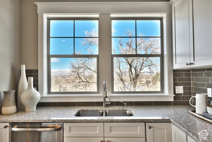 Dual-pane windows with grid detailing, speckled stone-finish countertops, stainless steel dual-basin undermount sink with arched pull-down faucet, gray horizontal subway tile backsplash, and shaker-style cabinetry