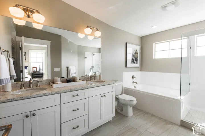 Double vanity featuring stone-finish countertops, undermount sinks, white shaker-style cabinetry, a built-in soaking tub with tile surround, and a glass-enclosed shower