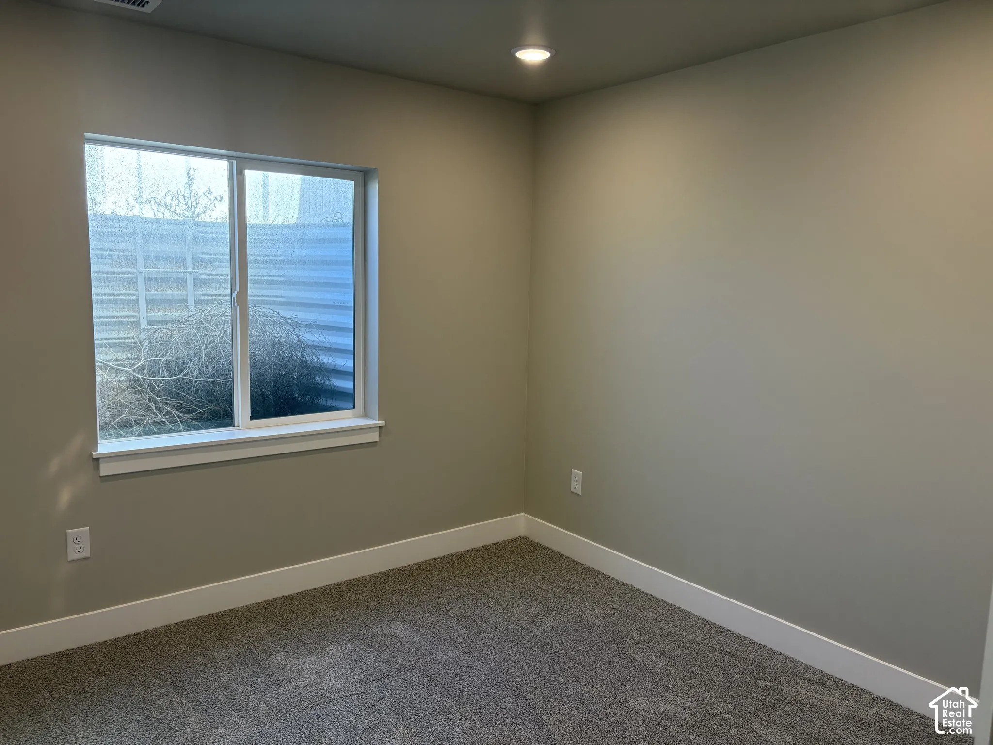 Neutral-toned interior space featuring wall-to-wall carpeting, recessed ceiling lighting, and a single-pane sliding window
