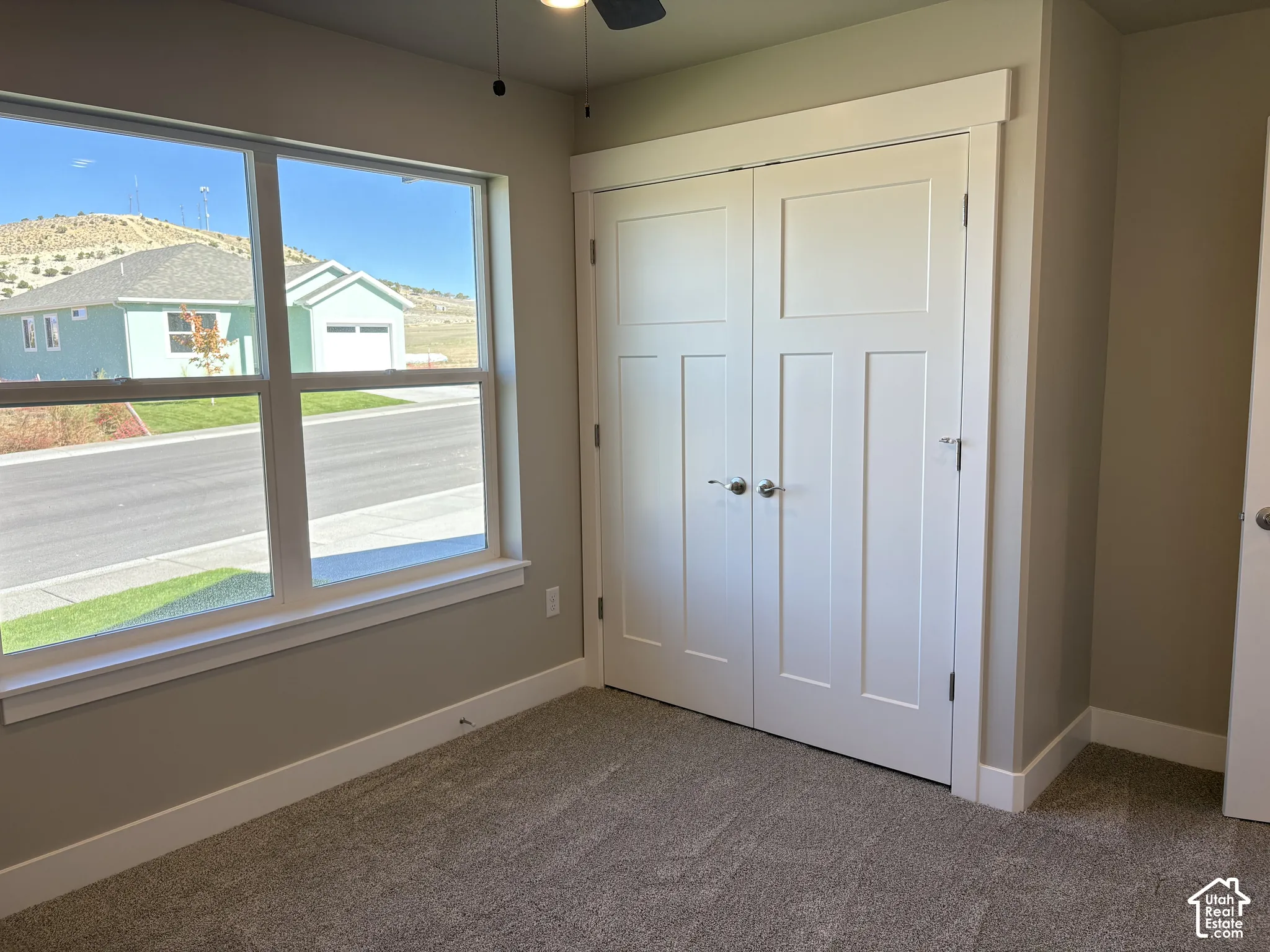 Room featuring double-panel closet doors, large window with sill, neutral wall paint, and ceiling-mounted fan