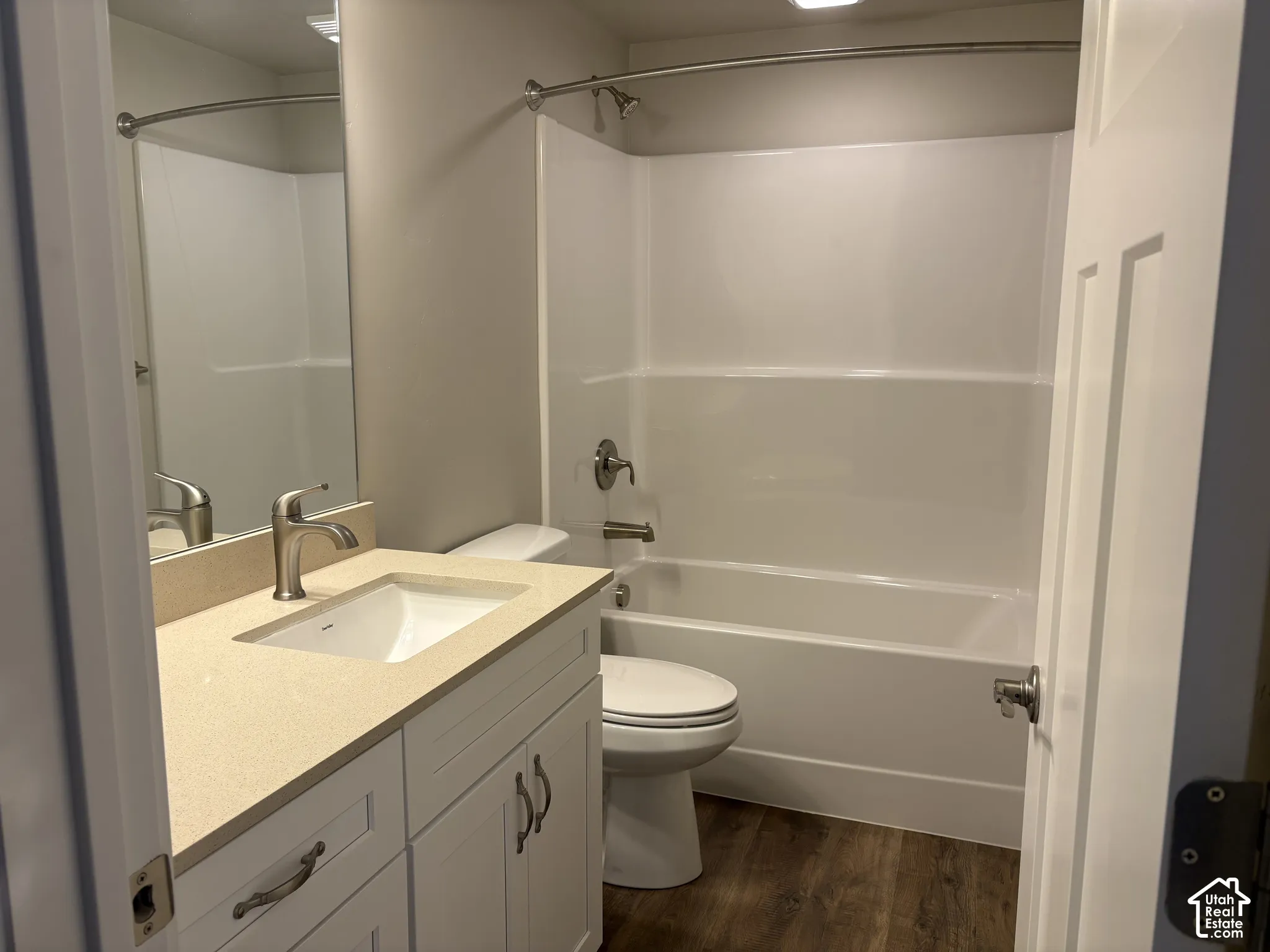 Bathroom featuring a white vanity cabinet, solid-surface countertop with an integrated rectangular sink, wood-finish flooring, and a tub-shower combination with a curved shower rod