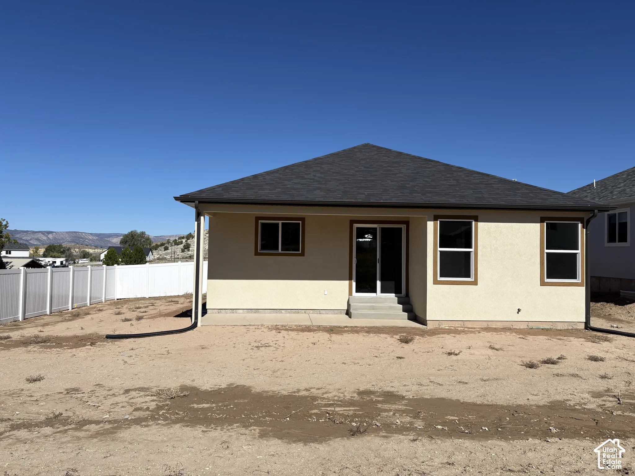 Single-story exterior featuring a hip roof, stucco siding, concrete patio, and white vinyl perimeter fencing