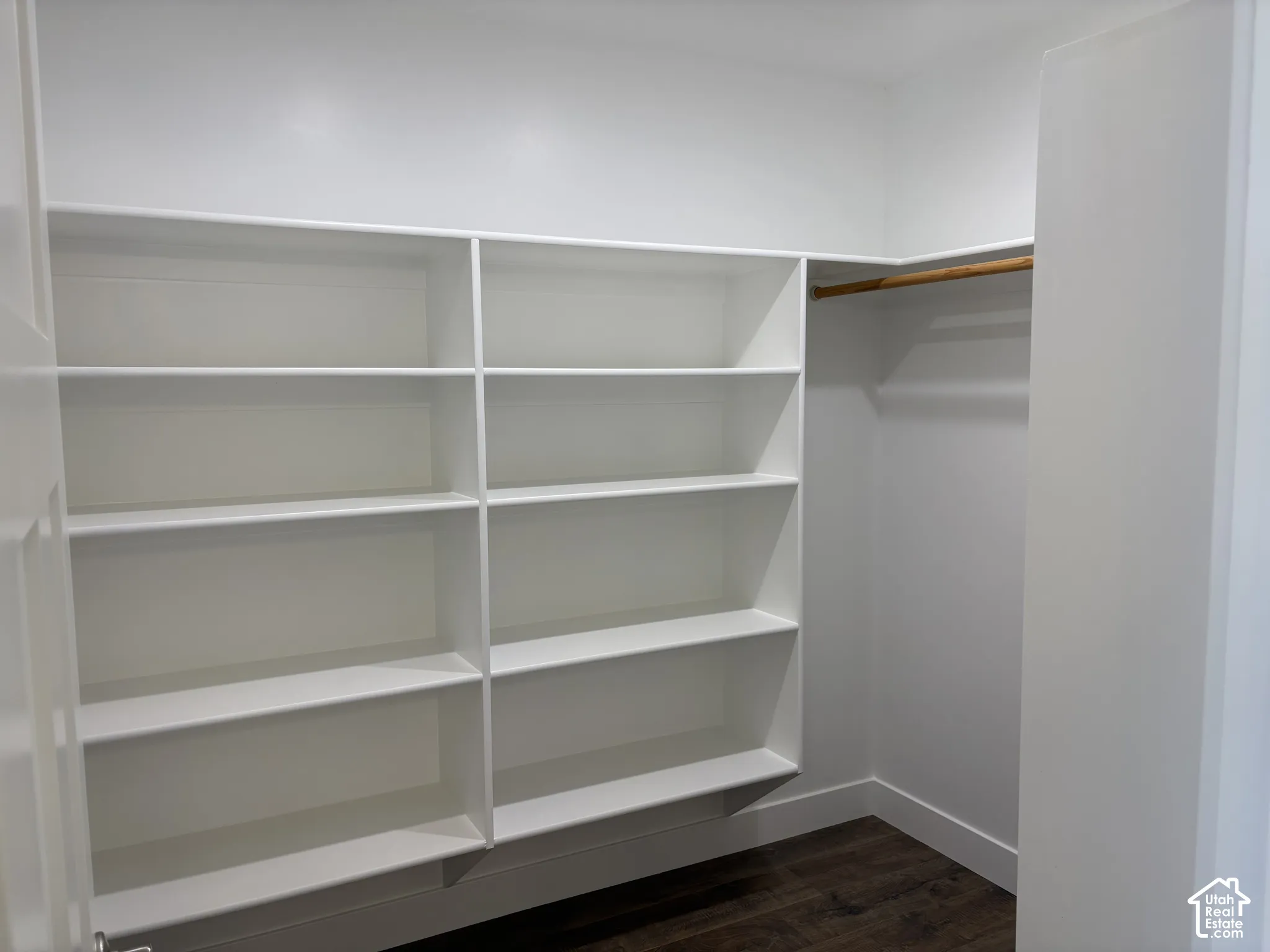 Custom walk-in storage featuring floor-to-ceiling white shelving, integrated rod for hanging garments, and wood-finish flooring