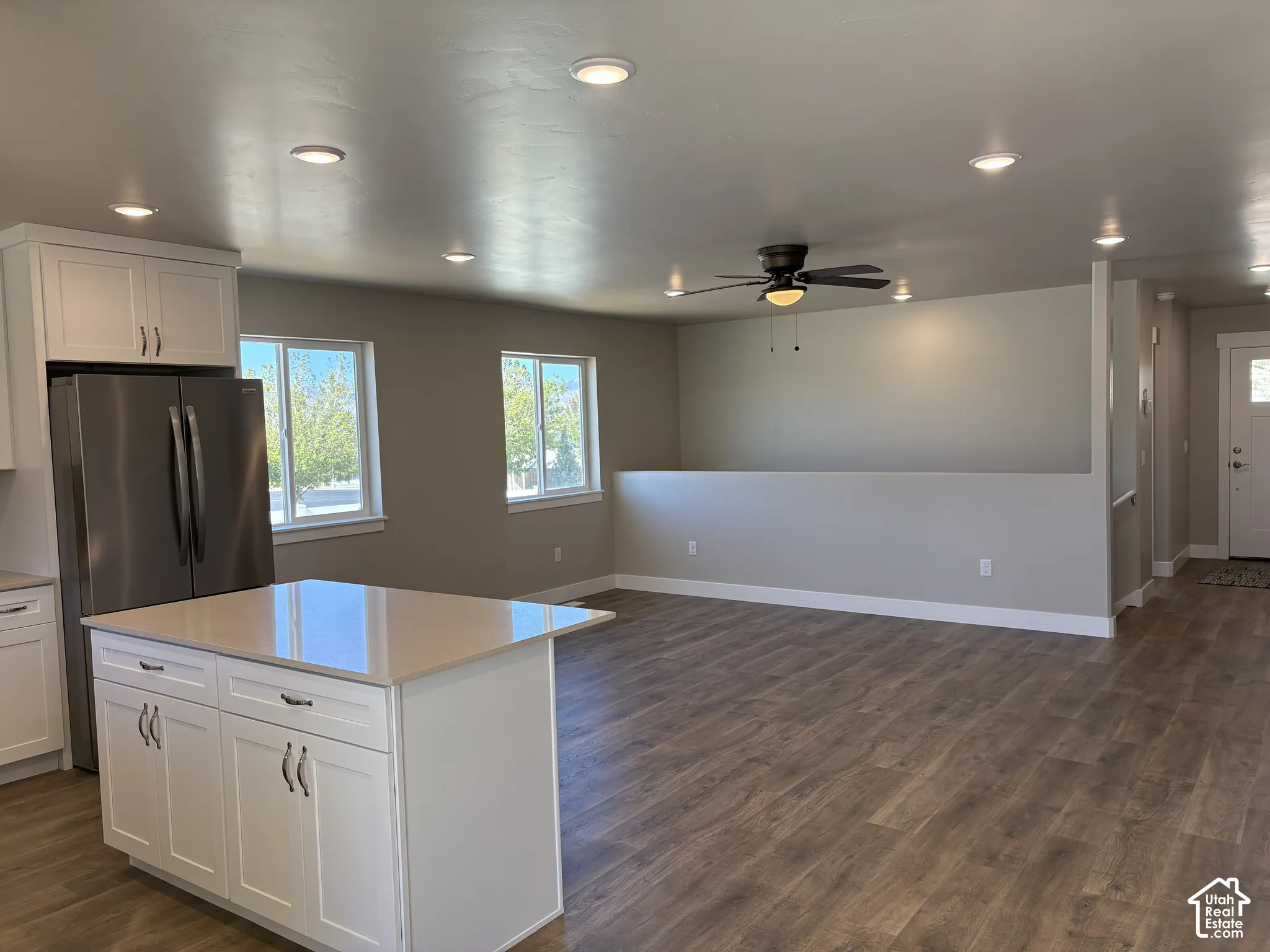 Kitchen featuring white shaker-style cabinetry, an island with stone-finish countertop, stainless steel refrigerator, recessed lighting, and wood-finish flooring