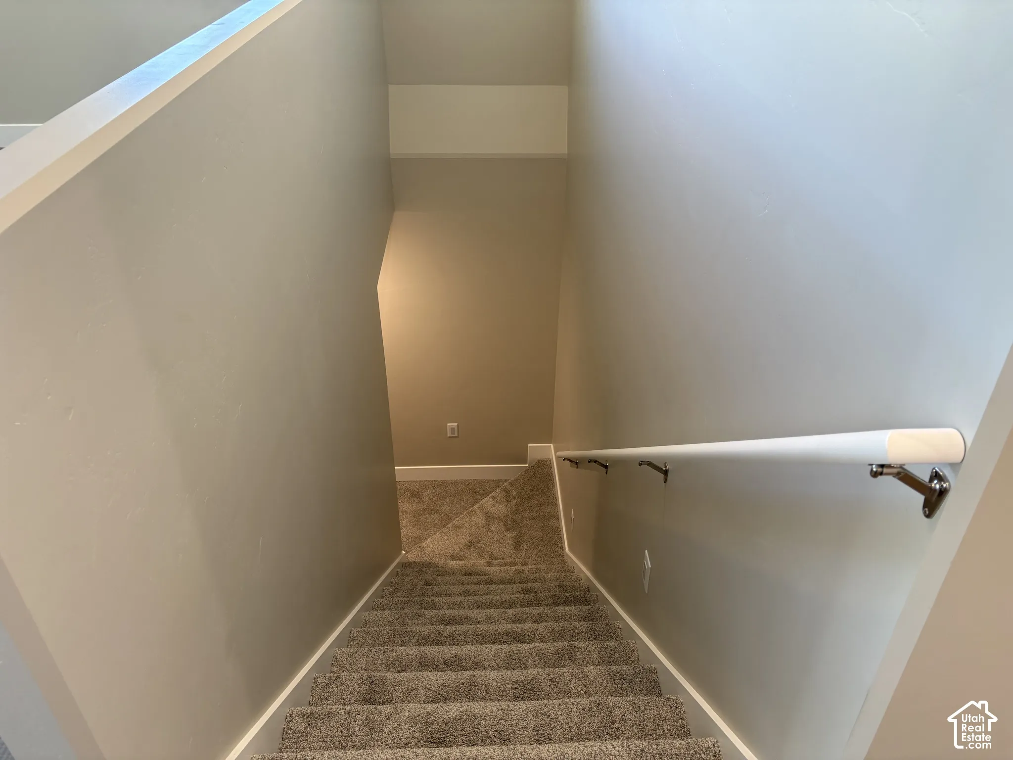 Stairway featuring neutral-toned carpeting and a white wall-mounted handrail with metal brackets