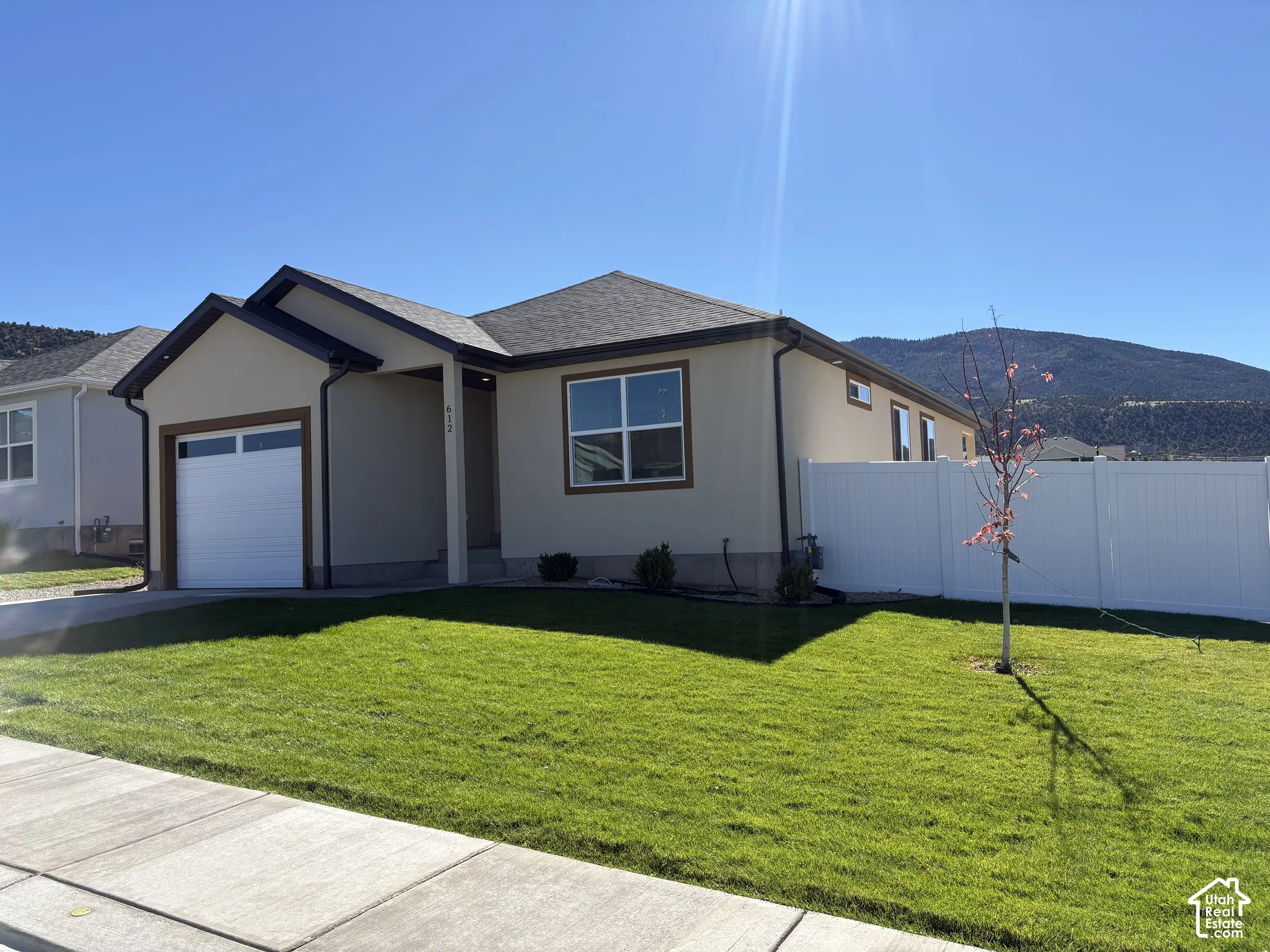 Single-story residence featuring a neutral stucco exterior, a single-car garage, and white vinyl perimeter fencing
